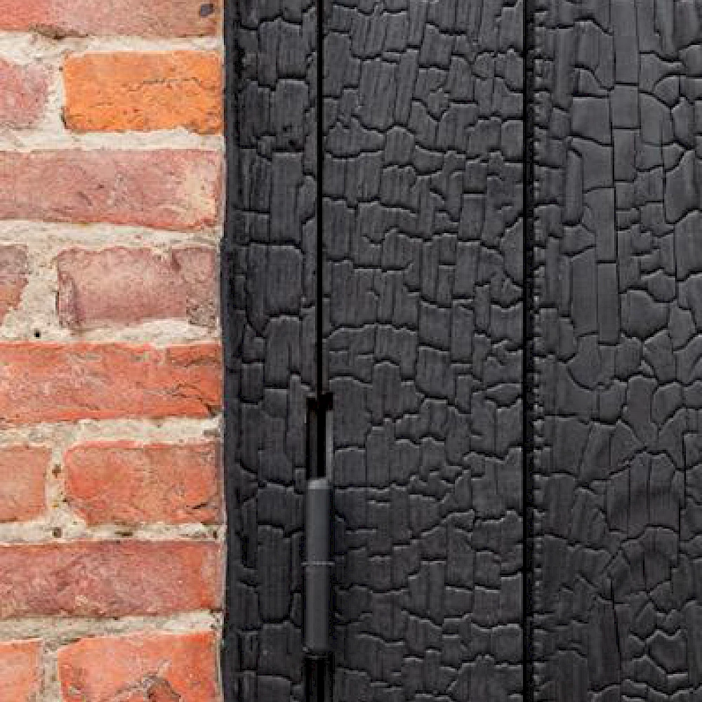 Close-up zwarte houten gevelbekleding naast bakstenen muur